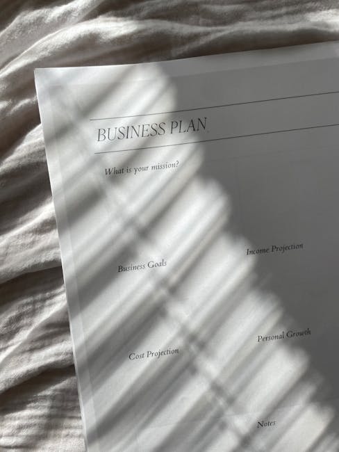 A printed business plan document titled 'BUSINESS PLAN' placed on a light-colored fabric surface, with natural sunlight casting shadows of nearby plants across the page. The document includes sections such as 'What is your mission?', 'Business Goals', 'Cost Projection', 'Income Projection', 'Personal Growth', and 'Nates'. The scene highlights a clean, organized workspace environment suitable for professional planning and business development, with no cleaning tools or surfaces visible in the image. Carpet Cleaners W8 emphasizes surface cleaning and sanitisation as part of their domestic cleaning services, ensuring hygiene and maintenance of work and living spaces.